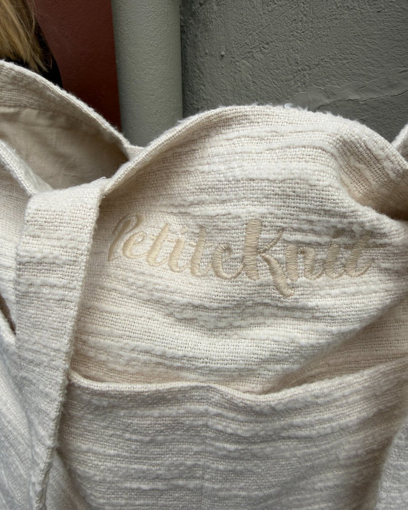Knitter's Shopper Light i farven Cloud stående på bænk med fokus på det broderede logo