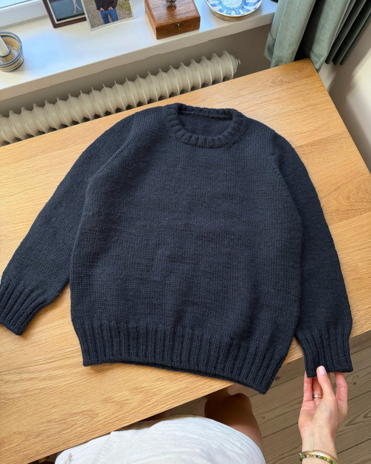 Blå Niels Sweater Junior liggende på skrivebord med fokus på den eropæiske skulderkonstruktion
