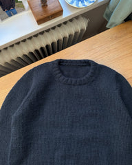 Blå Niels Sweater Junior liggende på skrivebord med fokus på halskanten