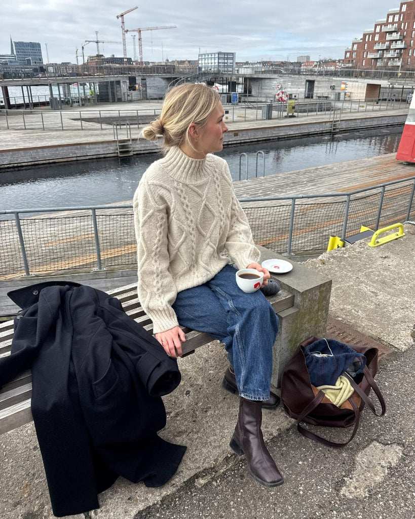 Siddende kvinde iført hvid Saga Sweater