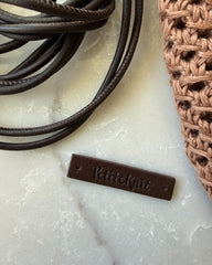 Skindsnøre og læderlabel med PetiteKnit-logo liggende sammen med Juno Satchel
