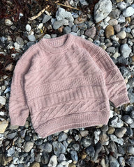 Lyserød Storm Sweater Junior liggende på strand med sten