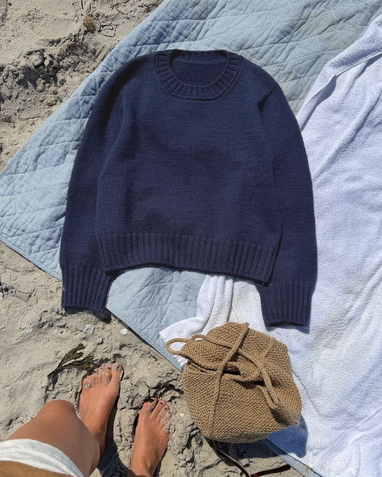 Blå Vega Sweater på strandtæppe med fokus på skulderen